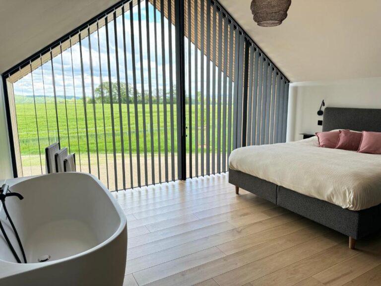 Chambre romantique moderne à Durbuy avec grande baie vitrée et baignoire îlot face à la nature.