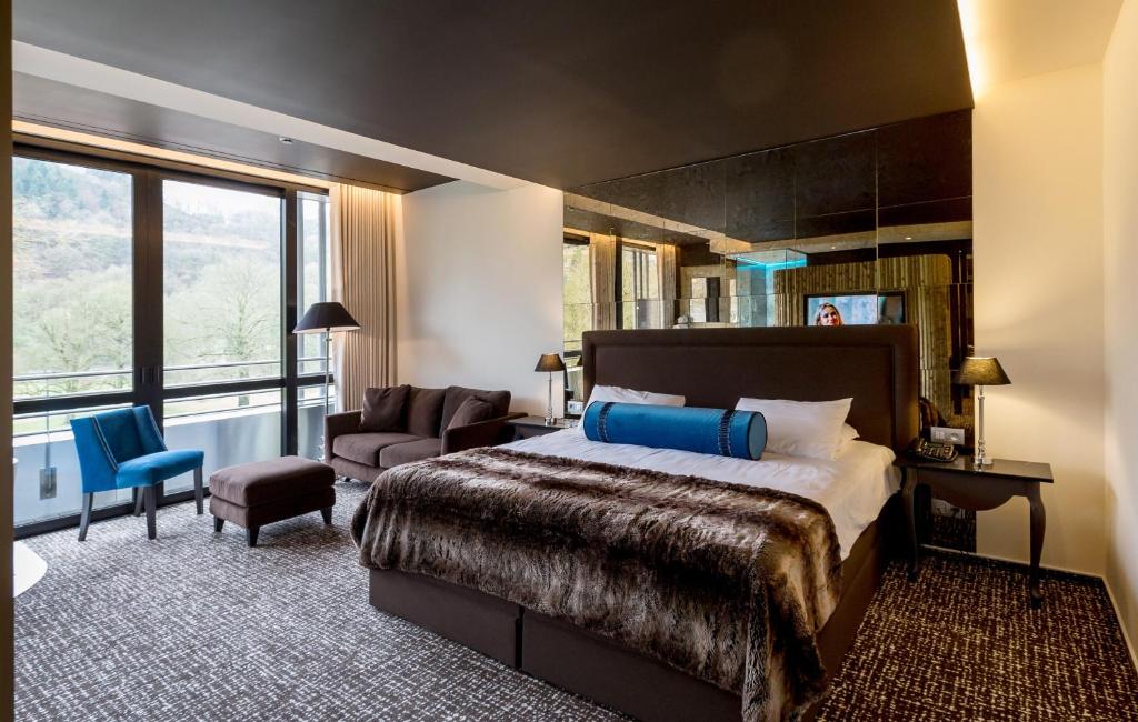 Chambre moderne et chaleureuse du Château des Thermes avec vue sur la nature, lit douillet et touches de bleu élégantes.